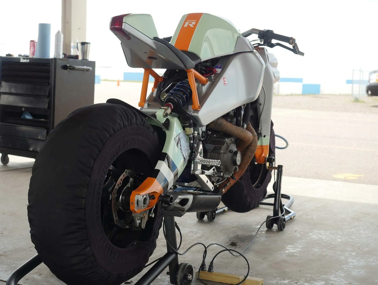 Unnumbered Ronin practice bike with tire warmers in a garage